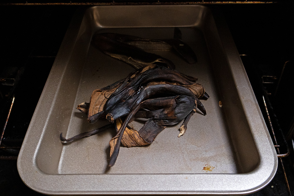 Cascas de banana escuras em uma bandeja de metal sendo colocadas no forno para ressecarem