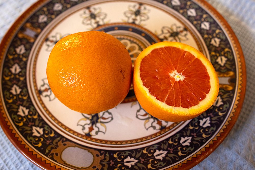 metade de uma laranja e uma laranja inteira em um prato de cerâmica estampado com arabescos