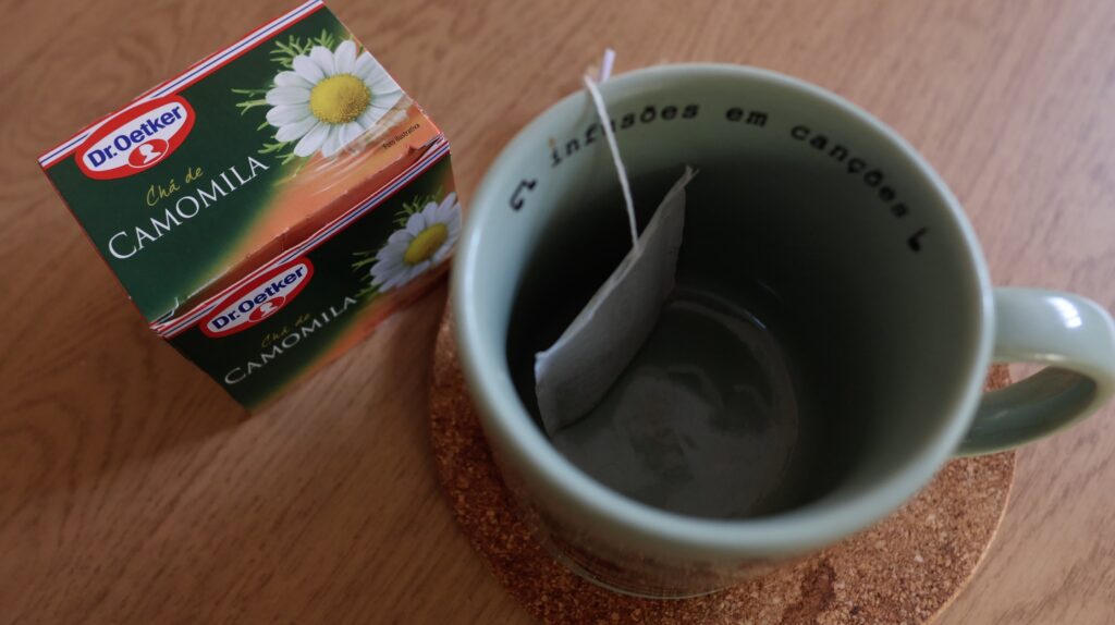 caixa de chá de camomila ao lado de uma xícara vazia com o sachê