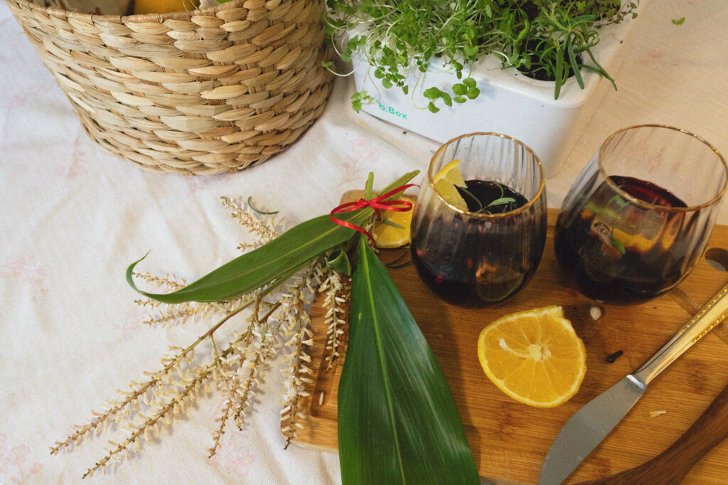 Taças de vinho sobre uma tábua de madeira com flores e rodelas de laranja, com uma B Box a Horta Inteligente da Brota Company ao laod